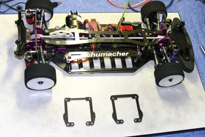 The small plates are used to change the car's roll center; typically a lower roll center for foam carpet racing, and higher for rubber or outdoors.  Also note the adjustable battery pack mount, allowing the battery to be angled towards the inside front of the car, while maintaining a low CG. (Click to enlarge)